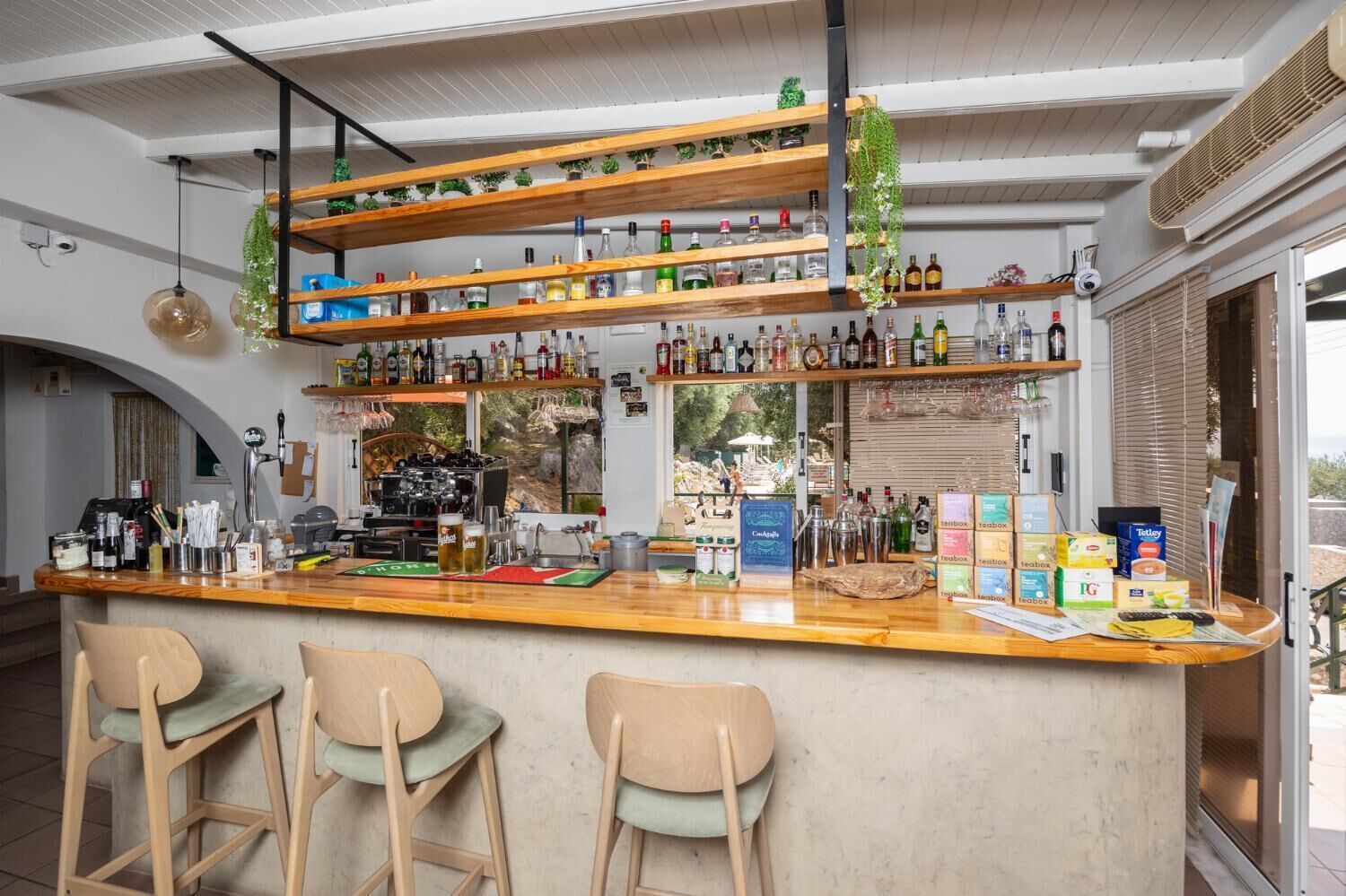 Un área de bar con estantes de madera llenos de botellas, una máquina de café y vistas al exterior.
