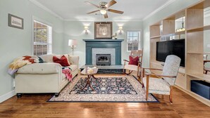 A living room with a fireplace, a ceiling fan, and a television. - University Place, family stay, practically on campus (Siloam Springs)