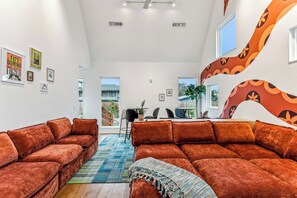 Un salon moderne doté d’un grand canapé d’angle, d’un coin repas avec une table et des chaises, et d’un escalier au design original.