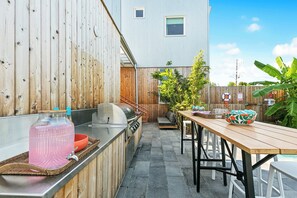 Une cuisine extérieure équipée d’un barbecue, d’un grand distributeur d’eau et d’une table à manger avec des chaises.