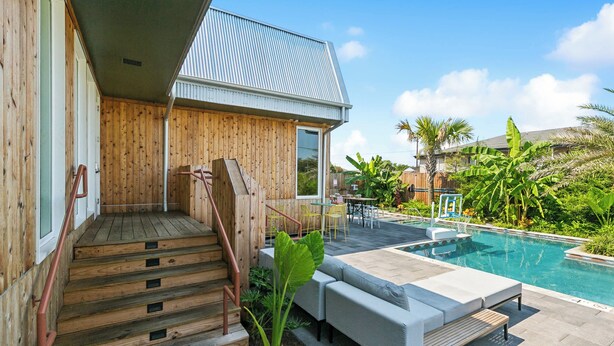 Una casa de madera con piscina, mobiliario exterior y una escalera que lleva a la entrada.