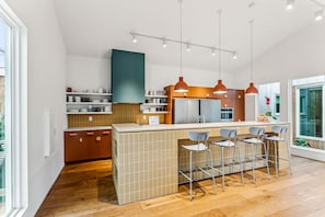 A modern kitchen with a central island, bar stools, pendant lighting, and a view of the outdoors.