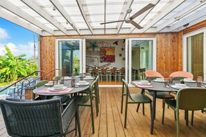 Un espace de restauration en plein air doté d’un plancher en bois, de chaises vertes et de tables prévues pour deux personnes.
