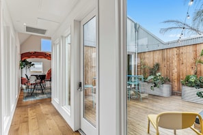 A modern interior with a wooden floor, a dining area with a table and chairs, and a view of a wooden fence and plants outside. - The Herald at CastleDay - Private Pool, Spa (New Orleans)