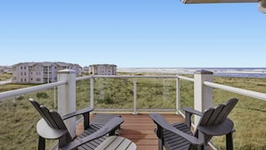 Un balcon avec deux fauteuils Adirondack donnant sur une plage et un bâtiment en arrière-plan.