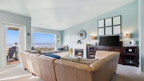 Un salon avec un canapé en cuir beige, une cheminée, un téléviseur et une vue sur l’océan par une grande fenêtre.