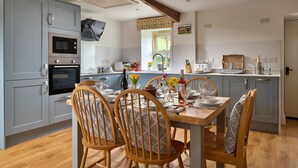 A modern kitchen with grey cabinets, a wooden dining table, and chairs. - Moelis Barn (Llandrillo)