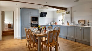 A modern kitchen with a dining area, featuring wooden chairs, a table set for four, and a built-in oven. - Moelis Barn (Llandrillo)