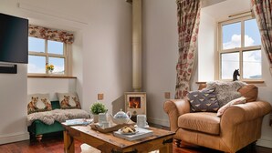 A cozy living room with a sofa, armchair, and a table with a teapot and cups. - Moelis Barn (Llandrillo)