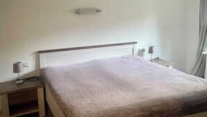 Ein Schlafzimmer mit einem Bett, Nachttischen, einer Lampe, einem Deckenventilator und einem an der Wand montierten Lichtschalter.