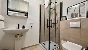 Ein modernes Badezimmer mit einer Duschkabine, einem Waschbecken, einer Toilette und einem Spiegel.