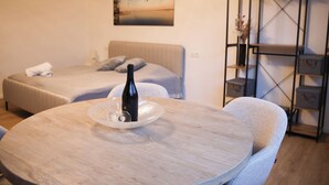 Ein Hotelzimmer mit zwei Betten, einem runden Holztisch mit einer Weinflasche und einer Wandablage mit Dekoration.
