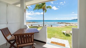 En overdækket terrasse med et træbord og stole, en palme og udsigt over havet.