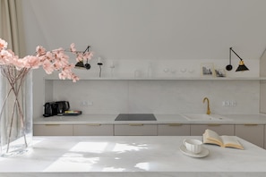 Une cuisine moderne avec un plan de travail blanc, une machine à café, un vase rempli de fleurs roses et un livre posé sur la table.