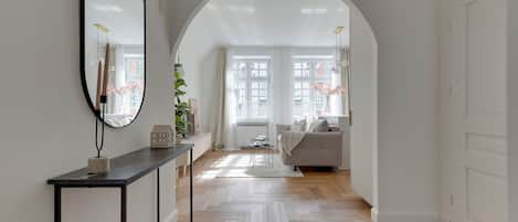 A hallway with a herringbone floor, a console table, a sofa, and a large mirror.