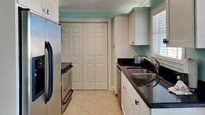 A kitchen with white cabinets, a stainless steel refrigerator, a double sink, and a window with blinds.