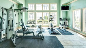 A gym with various exercise equipment, large windows, and a television mounted on the wall.