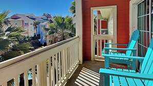 A balcony with turquoise chairs, a white railing, and a view of neighboring buildings.