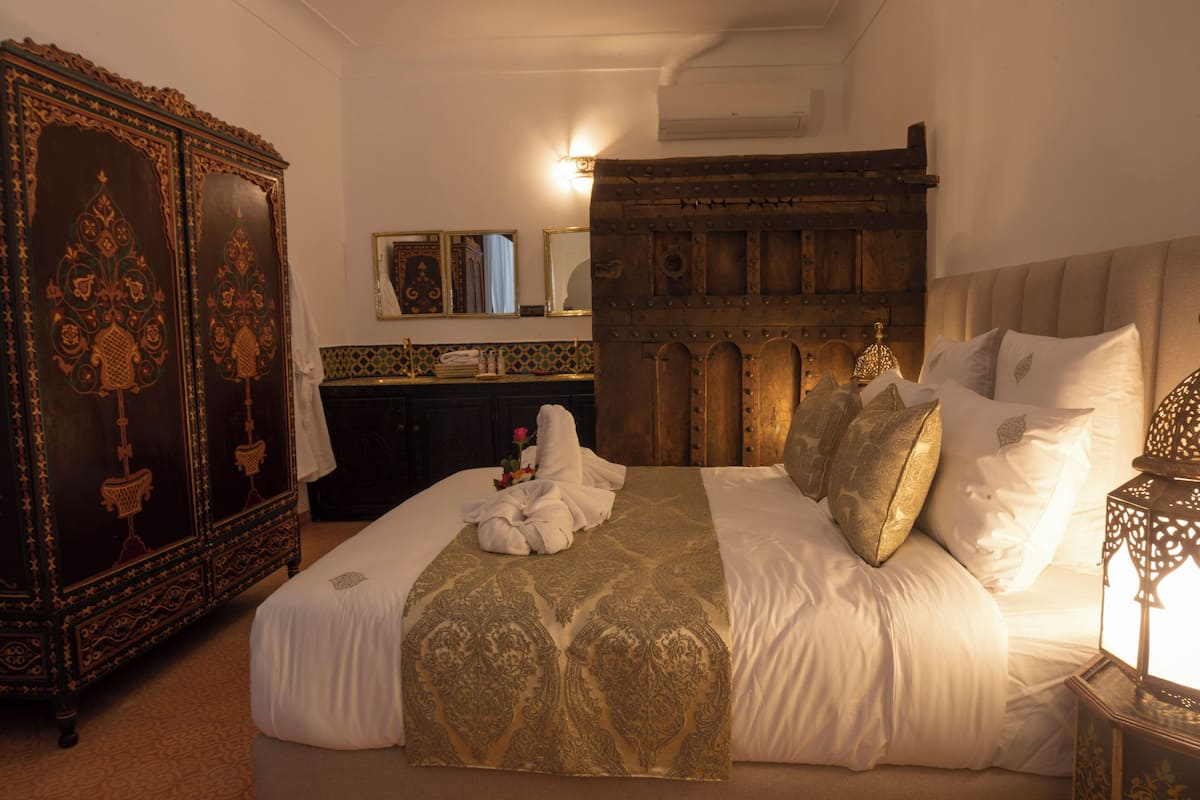 A bedroom with a large bed, a wooden wardrobe, and a nightstand with a lamp.