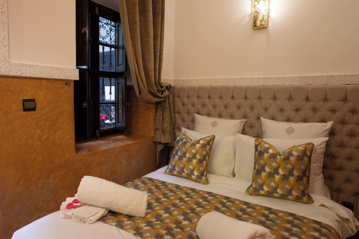 A bedroom with a tufted headboard, a patterned bedspread, and a window with curtains.
