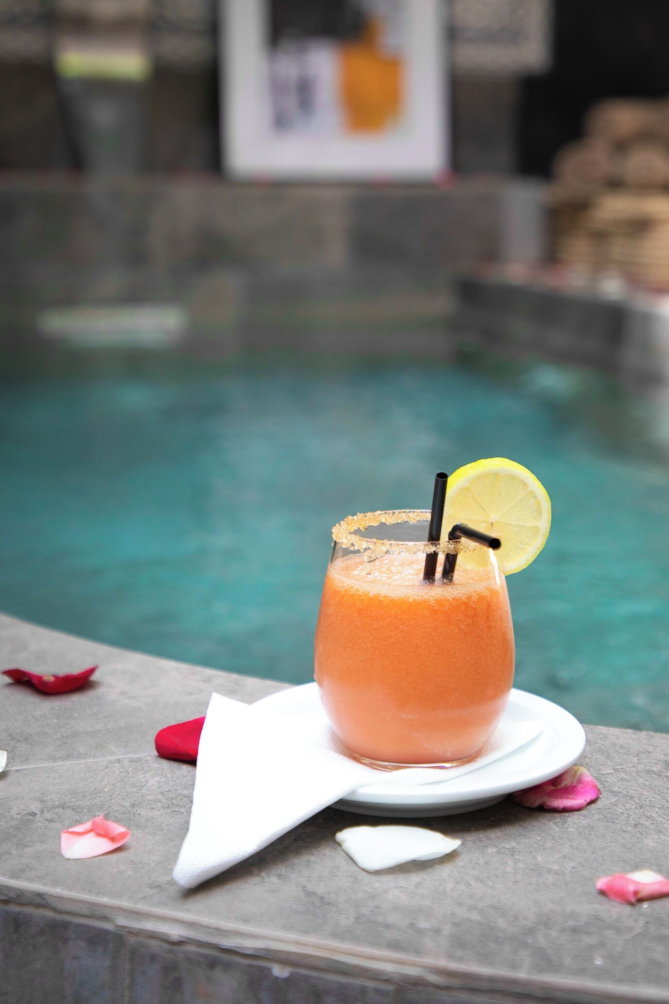 A cocktail with a lemon garnish on a stone ledge by a pool.