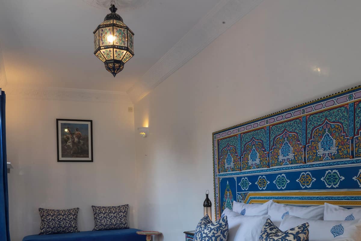 A neatly made bed with patterned bedding, a decorative headboard, and a hanging light fixture.