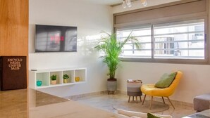 A modern living room with a large TV, a potted plant, a yellow armchair, and a bookshelf. - Luxury 3 bedroom apartment Agdal - 170 m2 by Masterhost (Rabat)