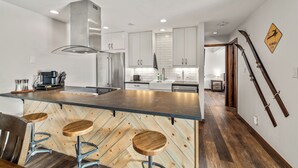 A modern kitchen with a central island, bar stools, stainless steel appliances, and a herringbone wood floor. - Modern Mountain Comfort at Timber Run 304! (Steamboat Springs)
