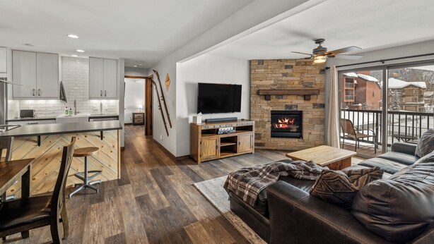 A modern kitchen with a dining area, a fireplace, and a living room with a leather sofa and a TV. - Modern Mountain Comfort at Timber Run 304! (Steamboat Springs)