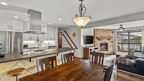 A modern kitchen with stainless steel appliances, a wooden dining table, and a stone fireplace. - Modern Mountain Comfort at Timber Run 304! (Steamboat Springs)