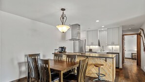 A modern kitchen with a central island, wooden dining table, and chairs. - Modern Mountain Comfort at Timber Run 304! (Steamboat Springs)