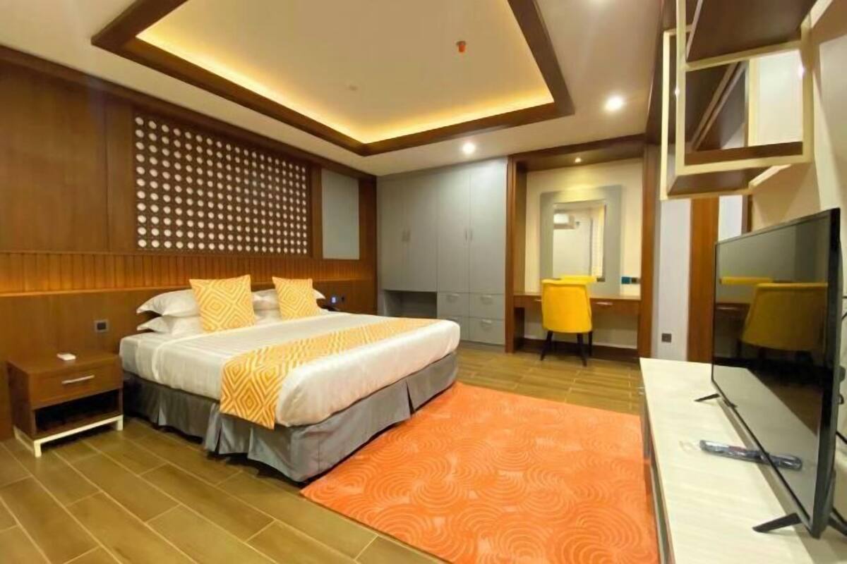 A modern hotel room with a bed, a desk, a television, and a bathroom.