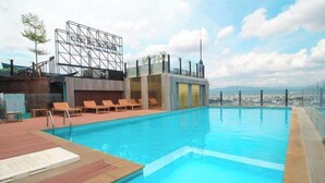 A rooftop pool with wooden lounge chairs and a view of the cityscape. - Holiday Pier Hotel (Mandalay)