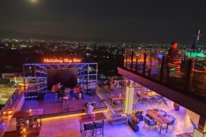 A rooftop bar with a stage, seating, and a city view. - Holiday Pier Hotel (Mandalay)