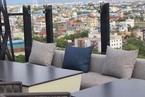 A sofa with a cushion, a table, and a view of a cityscape through a window. - Holiday Pier Hotel (Mandalay)