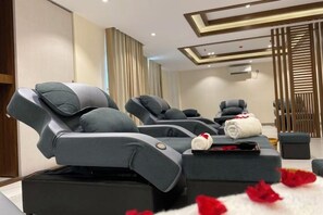 A massage therapy room with two massage chairs, a small table with towels, and a decorative wall panel. - Holiday Pier Hotel (Mandalay)