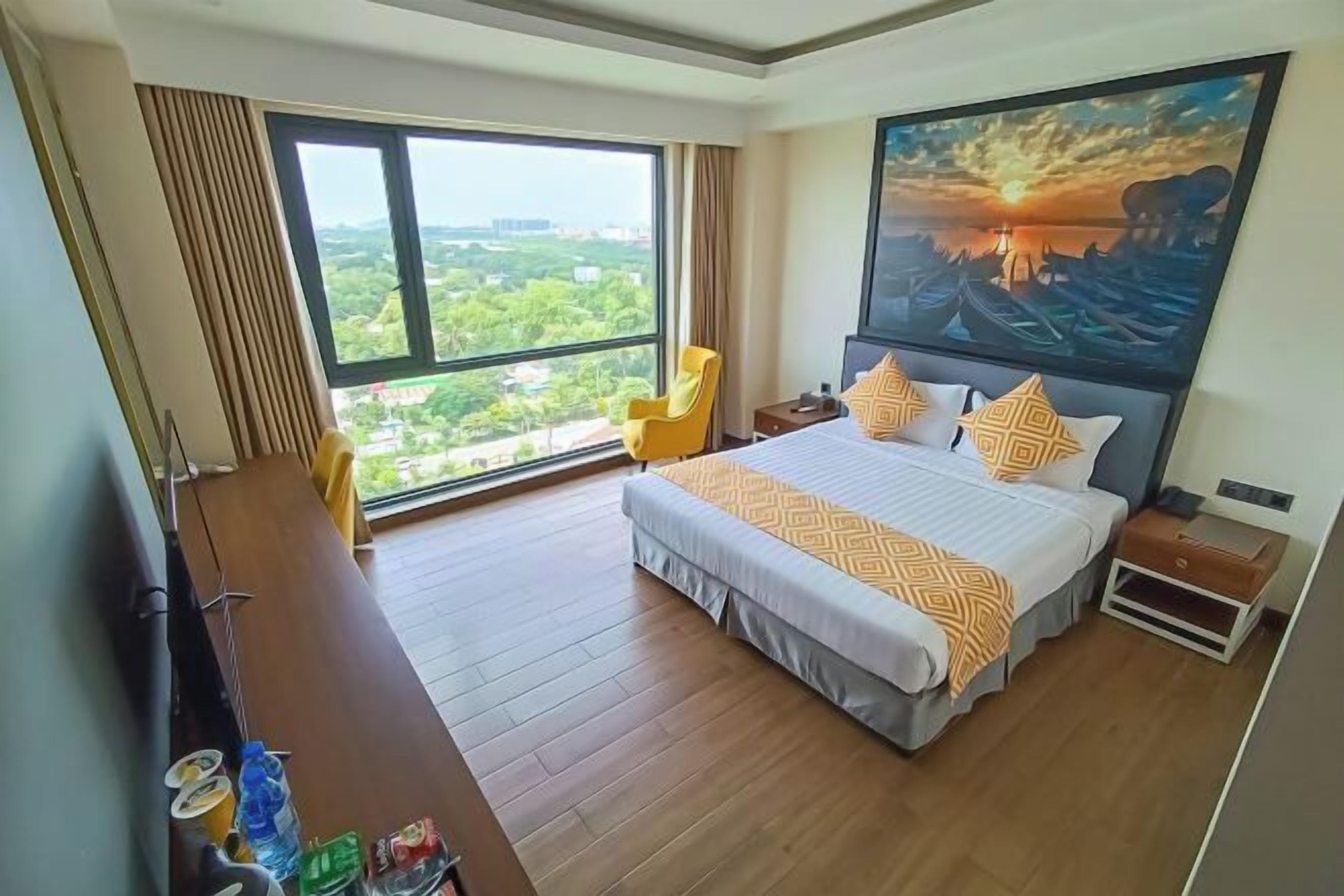 Habitación de hotel con una cama grande, un escritorio, una silla y un cuadro de un atardecer sobre el agua.