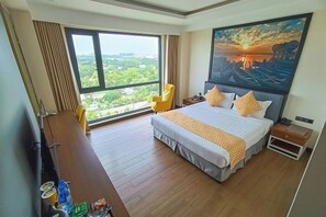 A hotel room with a large bed, a desk, a chair, and a painting of a sunset over water. - Holiday Pier Hotel (Mandalay)