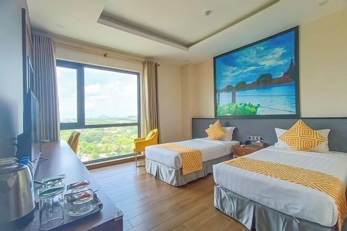 A hotel room with two beds, a desk with a coffee maker, and a large window.