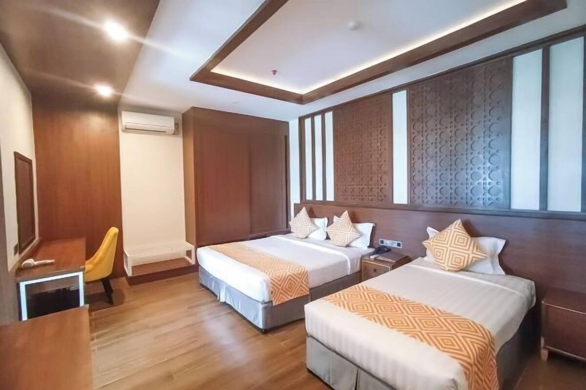 A hotel room with two beds, a desk, a chair, and a large window.