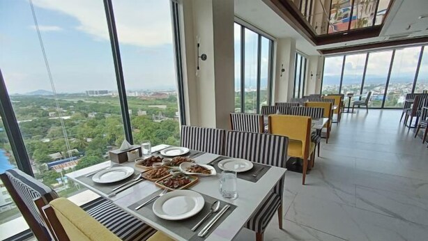 A dining area with a table set for four, large windows offering a city view, and modern striped chairs. - Holiday Pier Hotel (Mandalay)