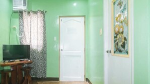 A room with a television, a patterned curtain, a white door, and a framed picture on the wall. - Zids Island Emprise Beach House (Pagudpud)