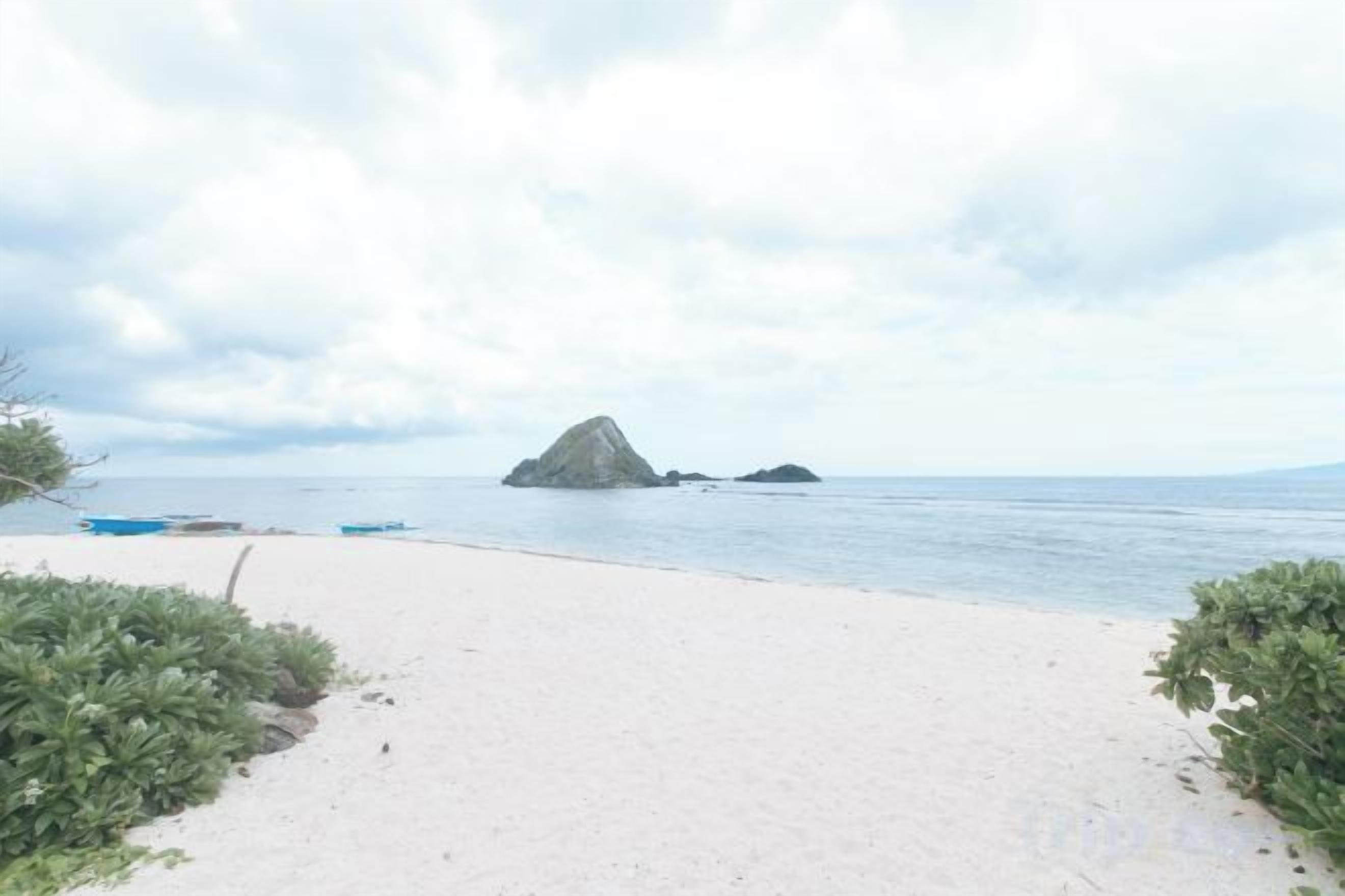 Una playa con un sendero arenoso que lleva al agua, una pequeña isla a lo lejos y un cielo despejado.