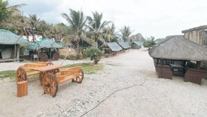A beachside village with thatched-roof huts and wooden furniture. - Zids Island Emprise Beach House (Pagudpud)