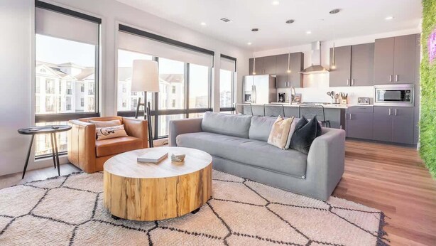 Una sala de estar moderna con un sofá gris, una mesa de centro redonda de madera y una mesita auxiliar.