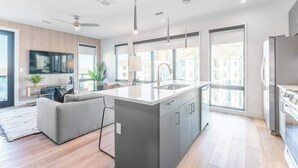 Una cocina moderna con una isla central, ventanas amplias y un sofá gris en un espacio luminoso.