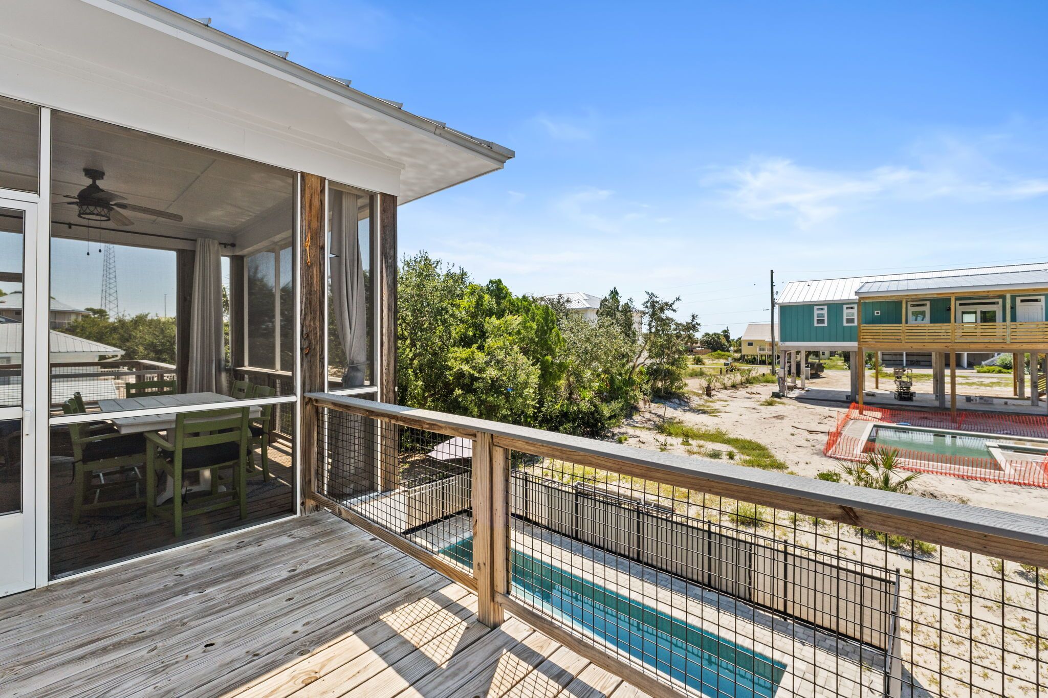 Une terrasse en bois avec une piscine, un patio couvert et une vue sur un bâtiment verdoyant et des arbres.