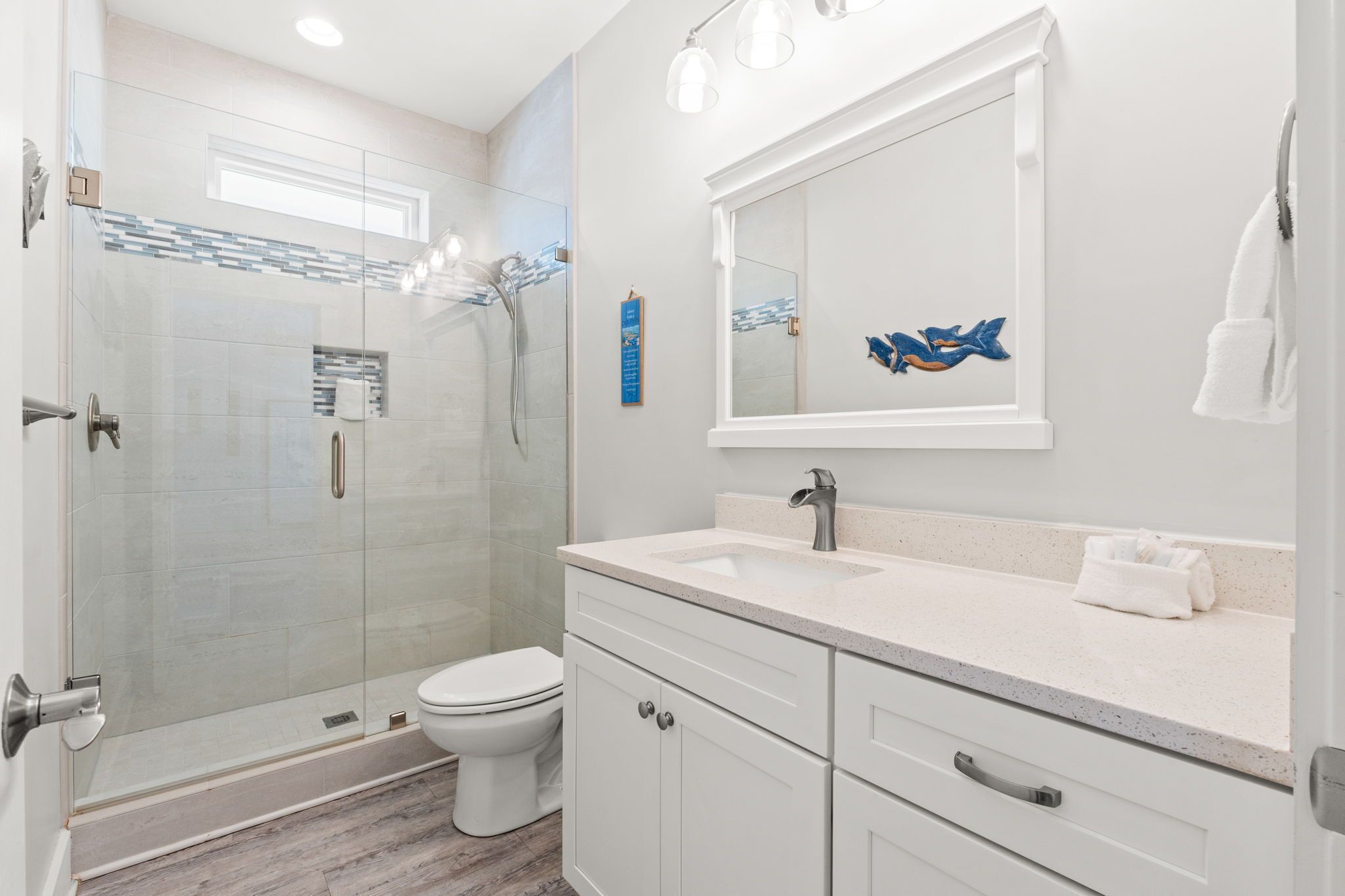 A modern bathroom with a glass-enclosed shower, a white toilet, and a vanity with a sink and mirror.