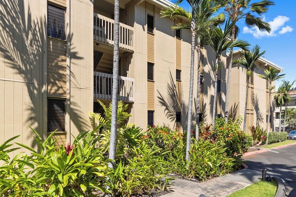 Un hotel de varios pisos con balcones, palmeras y un jardín bien cuidado.
