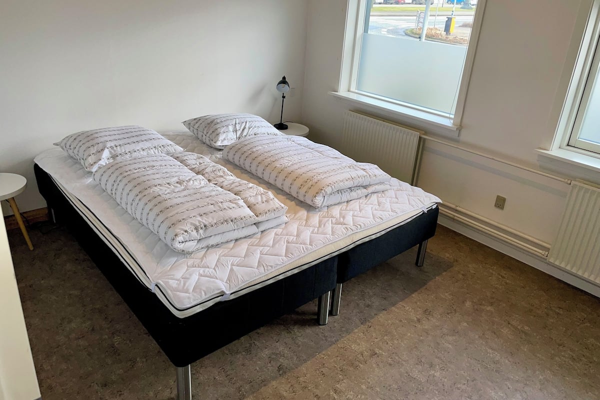 A room with two beds, a small table, and a window with a view of the street.